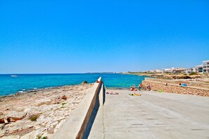 Un paseo marítimo con vistas al mar, una barandilla de hormigón y edificios al fondo.