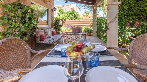 An outdoor dining area with wicker chairs, a table set for two, and a view of the surrounding garden and buildings. - CASA PIEDRA MALLORCA (Son Ferrer)