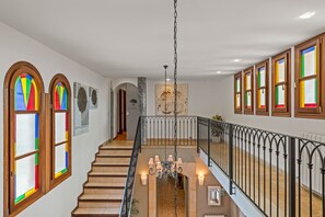 A multi-level interior with a staircase, stained glass windows, and a chandelier.