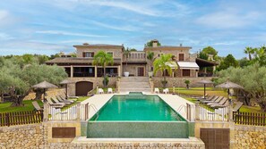 A large stone house with a swimming pool, outdoor seating, and a well-maintained garden.