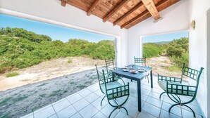 Un patio cubierto con una mesa y sillas, ventanas amplias y vistas a un paisaje natural.