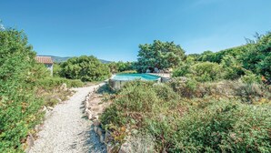 Una piscina rodeada de vegetación, un sendero de piedra y un edificio con tejado de tejas rojas.