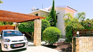A white car parked in front of a house with a stone pillar, a wooden pergola, and a metal fence. - Villa Olivia (Coral Bay)