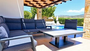 A modern outdoor seating area with a pool, stone walls, and a view of the landscape. - Villa Olivia (Coral Bay)