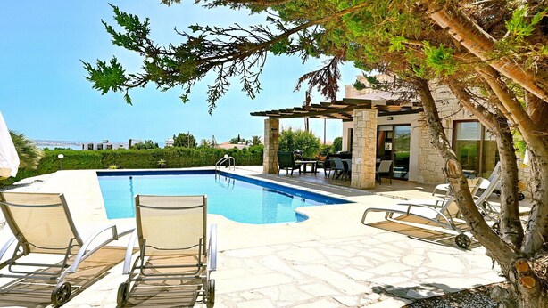 A swimming pool with lounge chairs, a pergola, and a view of the sea. - Villa Olivia (Coral Bay)