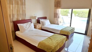 A hotel room with two beds, a nightstand, a lamp, and a view of the outdoors. - Private Detached Villa With Pool Ideal for Families (Coral Bay)