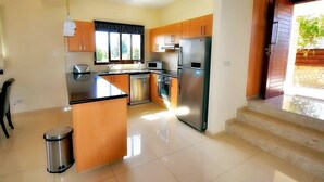 A modern kitchen with wooden cabinets, stainless steel appliances, and a black countertop. - Villa Olivia (Coral Bay)