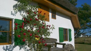 Ein traditionelles Haus mit einem Reetdach, Holzläden und einer Bank davor.