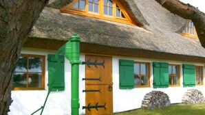 Ein traditionelles Haus mit einem Strohdach, einer Holztür und grünen Fensterläden.