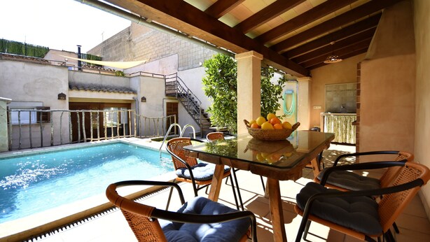 Zona de piscina con mesa de vidrio, sillas de mimbre y frutero.