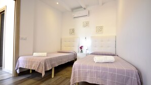 Habitación de hotel con dos camas, cada una con cabecero y almohada. Hay una mesita de noche con una lámpara y un florero.