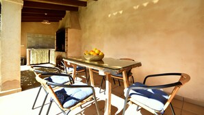 Un área de comedor rústica al aire libre con chimenea de piedra, sillas de mimbre y una mesa con frutero.