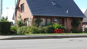 A brick house with a dark tiled roof, a small window, and a red bench in the front yard.