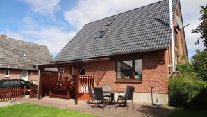 A brick house with a tiled roof, a covered patio with a table and chairs, and a car parked in the driveway.