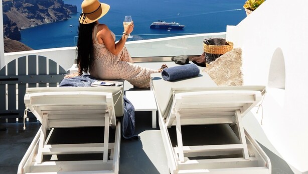 A woman sitting on a balcony with a view of the sea and a ship. - "Ethereum Luxury Cave" private jacuzzi villa in Imerovigli  (Santorini)