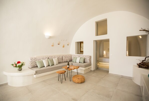Una sala de estar moderna con una pared blanca curva, un sofá seccional con cojines estampados, una mesa de centro de madera y una mesita auxiliar con un florero.