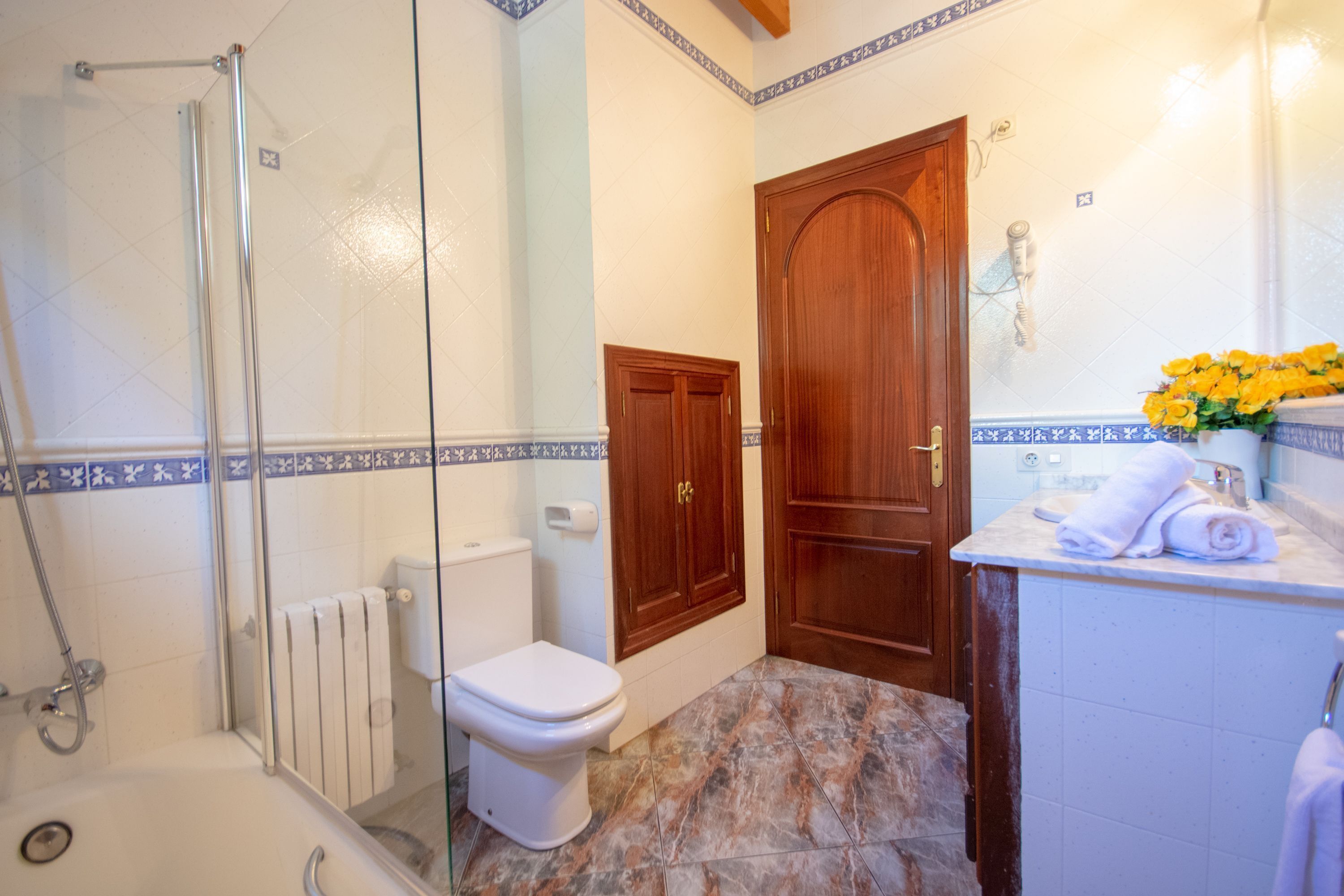 Ein Badezimmer mit Duschkabine aus Glas, Toilette, Holztür und Waschbeckenbereich mit Handtuch.