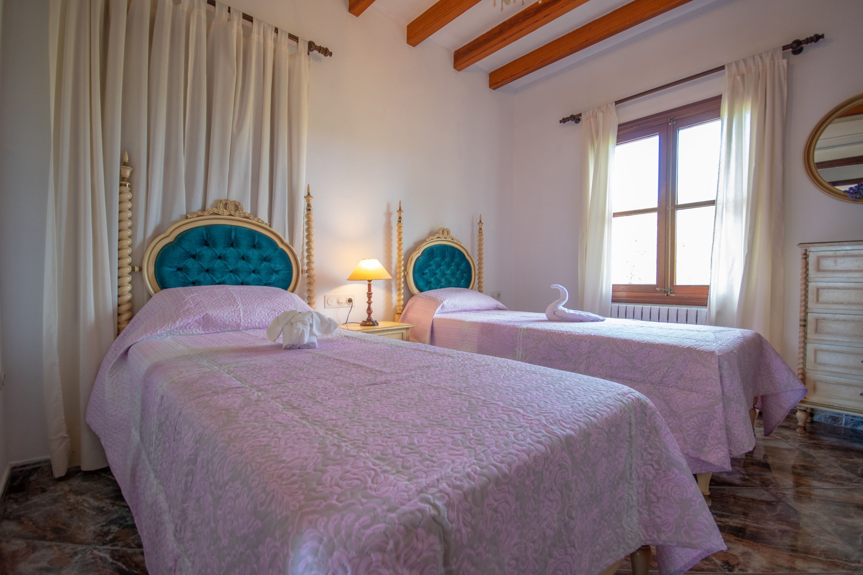 A hotel room with two beds, a wooden ceiling, a window with curtains, and a white dresser.