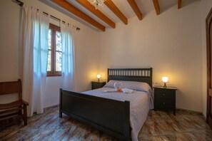 A bedroom with a wooden bed, two bedside tables with lamps, a bench, and a window with curtains.