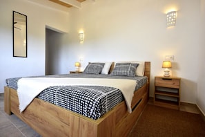 A bedroom with a wooden bed, two bedside tables with lamps, a mirror, and a wall-mounted light fixture.