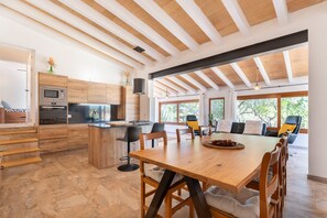 A modern kitchen with wooden cabinetry, a central island, and a dining area with a large table and chairs.