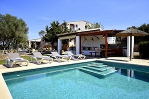 A pool with lounge chairs, a pergola, and a thatched umbrella.