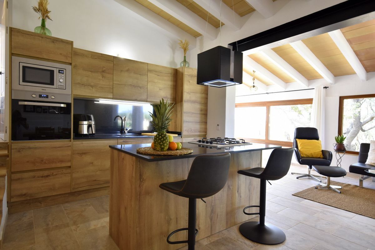 Una cocina moderna con armarios de madera, una isla integrada con taburetes de bar, estufa a gas y microondas.