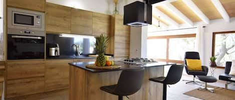 A modern kitchen with wooden cabinetry, a built-in island with bar stools, a gas stove, and a microwave.
