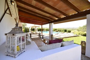 Ein überdachter Außenbereich mit Pool, Laterne und einer Couch.
