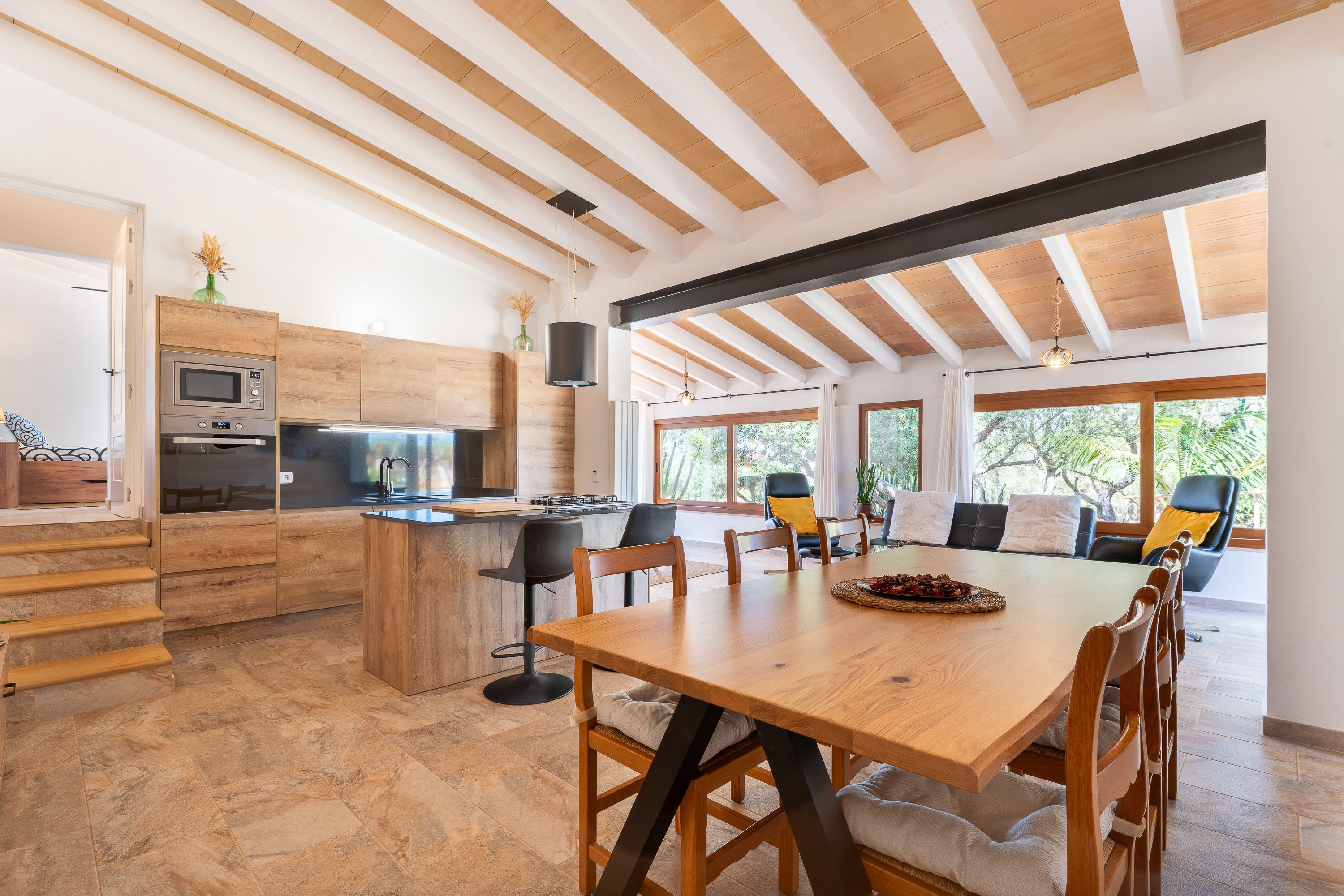 A modern kitchen with wooden cabinetry, a central island, and a dining area with a large table and chairs.