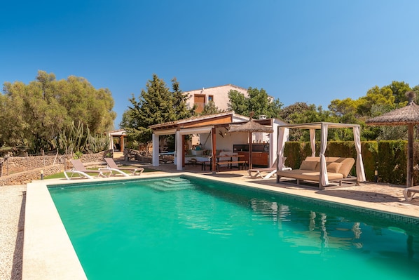 A pool area with lounge chairs and a covered seating area.