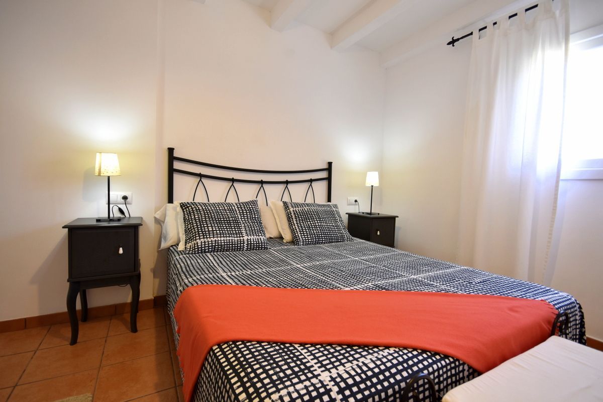Una camera da letto con un letto, due comodini, una lampada su ciascun comodino, una finestra con tende e un pavimento piastrellato.