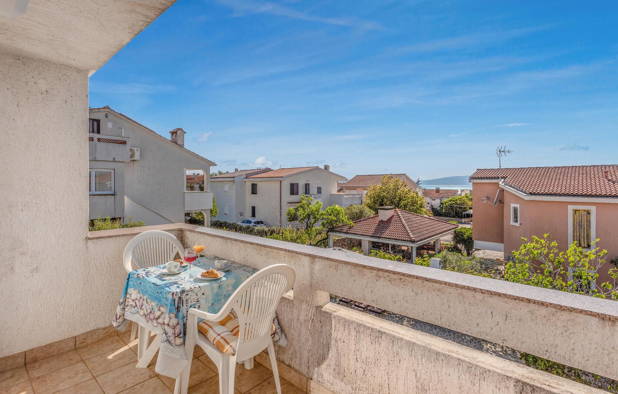 A balcony with a table and chairs, overlooking a residential area with houses and a clear sky.