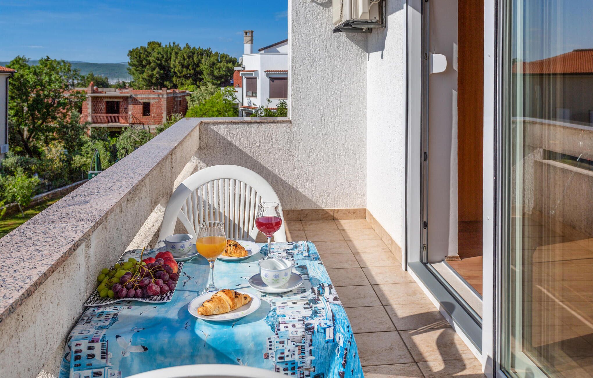 A balcony with a table set for breakfast, including croissants, grapes, and a glass of orange juice.