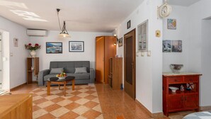 Un soggiorno con divano, tavolino e mobiletto in legno. Si nota una porta che dà su un'altra stanza e un orologio appeso al muro.