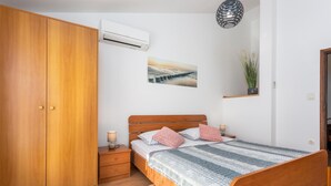 Una camera da letto con un'armadio in legno, un letto con coperta a righe, un comodino con una lampada e un condizionatore d'aria a parete.