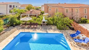 Una piscina con lettini, una zona barbecue e vista su edifici residenziali.