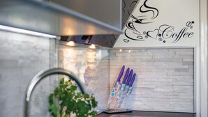 Une cuisine avec un pare-feu en pierre, un motif décoratif mural sur le thème du café et un bloc à couteaux doté de manches colorés.