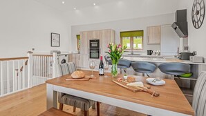 A modern kitchen with a wooden table, bar stools, and a dining area.