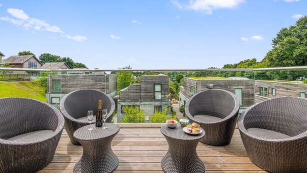 A terrace with wicker furniture, a bottle of champagne, and a bowl of fruit.