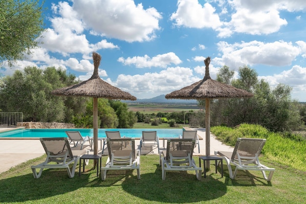 A poolside area with lounge chairs and thatched umbrellas, overlooking a scenic landscape.
