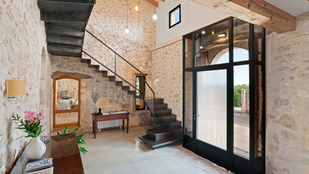Ein geräumiger Raum mit Steinsandsteinwand, einer Holztreppe, einem Klavier und einer großen Glasdoor, die nach draußen führt.