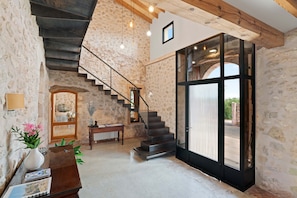 A spacious room with a stone wall, a wooden staircase, a piano, and a large glass door leading outside.