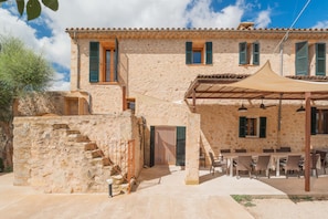 A stone building with a terrace, outdoor seating, and a staircase leading to the entrance.
