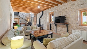 Ein rustikales Interieur mit freiliegenden Holzbalken, Steinwänden, einem Kamin und einer gemütlichen Sitzecke mit Sofa und Couchtisch.