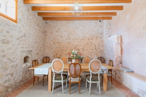 A rustic dining room with a wooden table and chairs, stone walls, and a hanging light fixture.