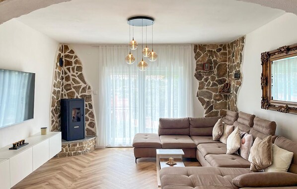 A living room with a stone accent wall, a large sofa, a television, and a fireplace. - Nice apartment in Srinjine (Srinjine)