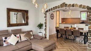A modern living room with a sectional sofa, a dining area with a wooden table and chairs, and a kitchen with stone accents. - Nice apartment in Srinjine (Srinjine)