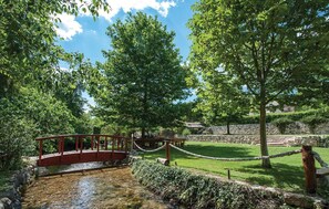 Cross a tranquil bridge over a serene stream surrounded by lush greenery and mature trees.