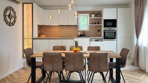 A modern kitchen with a dining area, featuring a wooden table, six chairs, pendant lights, and built-in appliances. - Nice apartment in Srinjine (Srinjine)